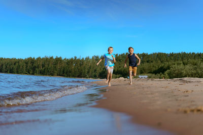 Rear view of woman walking on beach against blue sky