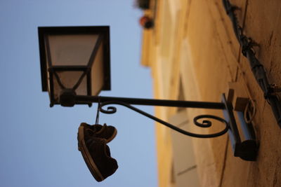 Low angle view of electric lamp hanging against sky