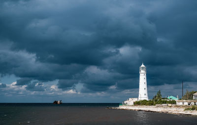 Lighthouse and buildings by sea against sky