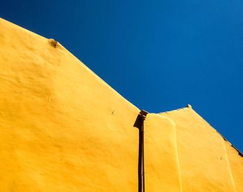 Low angle view of yellow flag against clear blue sky