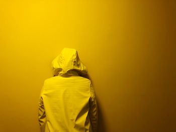 Rear view of person wearing hooded shirt standing against yellow wall
