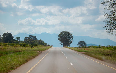 Empty road along landscape and trees against sky