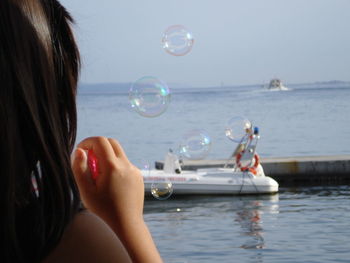 Close-up of teenage girl blowing bubbles at sea against sky