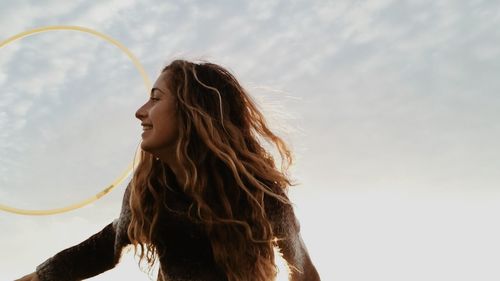 Low angle view of young woman with plastic hoop against sky