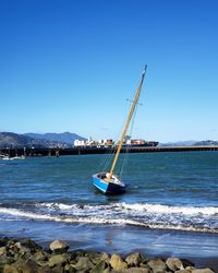 Sailboat moored on sea against clear blue sky