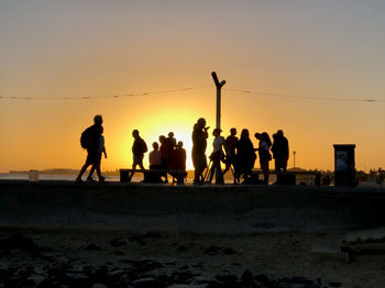 Silhouette people on beach against sky during sunset