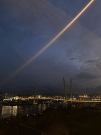Illuminated city by river against sky at night