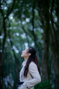 Side view of mid adult woman looking up while standing against trees in forest