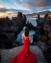 Rear view of woman wearing red dress while standing on cliff