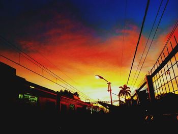 Low angle view of electricity pylon against sky at sunset