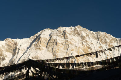 Low angle view of snowcapped mountains against clear blue sky