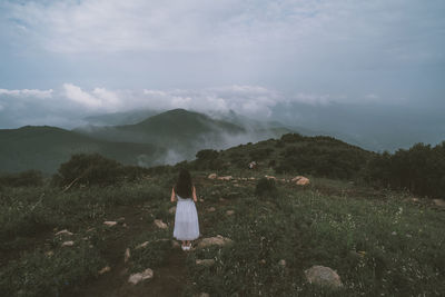 Rear view of woman standing on mountain against sky