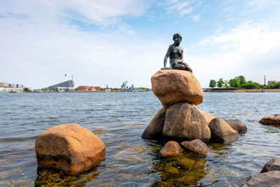 Statue on rock by sea against sky