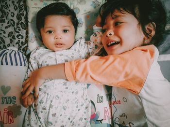 Cute baby girl with sister lying on bed at home