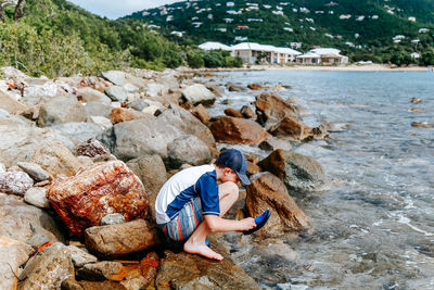 Side view of man sitting on rock at beach