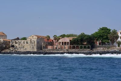 Buildings by sea against clear blue sky