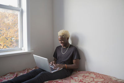 A young man sitting on a bed with a laptop