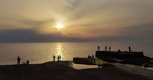 Silhouette people on beach against sky during sunset