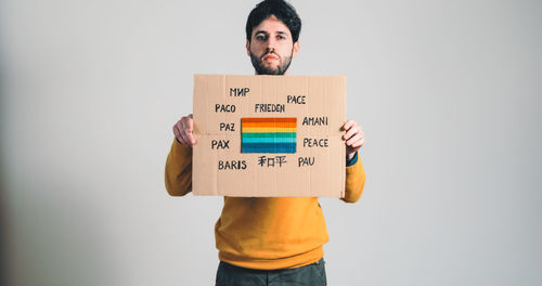 Portrait of young man holding placard against wall