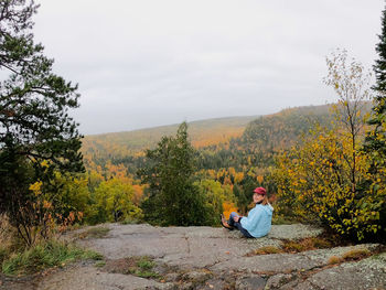 Man sitting on plants by trees against sky