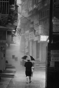 Rear view of man walking in a heavy rain with black umbrella 