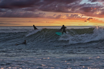 People in sea against sky during sunset