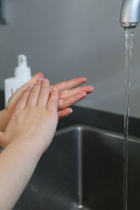 Close-up of hand touching water from faucet at home
