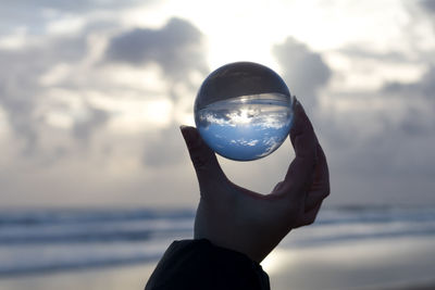 Close-up of hand holding crystal ball against sea