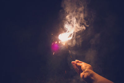 Close-up of hand holding illuminated sparkler against sky at night