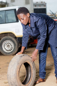 Young female mechanic holds a backup tire for spare in a car workshop.