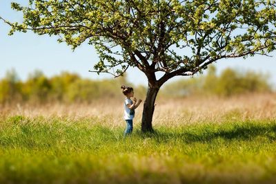 Side view of girl standing on field by tree