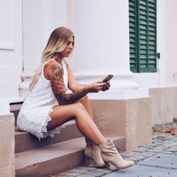 Fashionable woman using phone while sitting on staircase outdoors