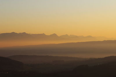 Scenic view of silhouette mountains against orange sky