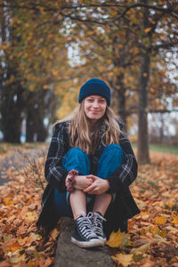 Smiling girl sit in a pile of colour leaves in city park. candid portrait of woman in autumn clothes