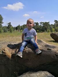 Boy sitting on rock against sky