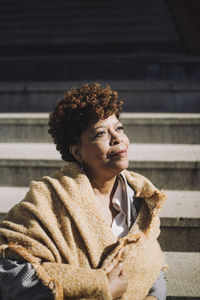 Contemplative senior woman with curly hair sitting on steps during sunny day