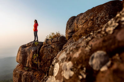 Low angle view of woman standing on rock against sky