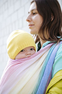 Mother holding baby wrapped in blanket looking away on sunny day