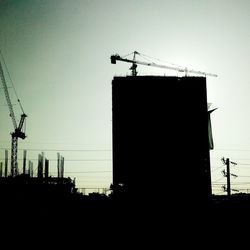 Low angle view of silhouette cranes against sky at dusk