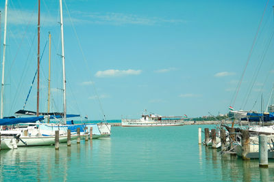 Sailboats moored in river against sky on sunny day