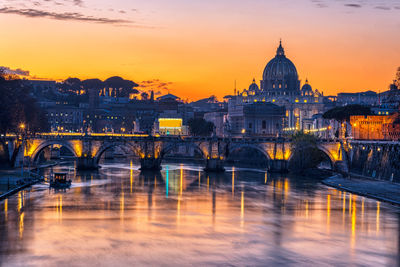 Bridge over river and buildings against sky during sunset