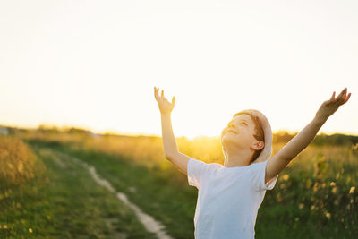 Portrait of a boy in a white t-shirt raising his hands up and playing and having fun on the field