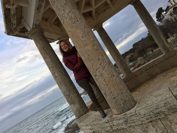 Full length of happy woman standing in gazebo by sea