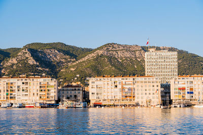 Buildings by river against clear sky