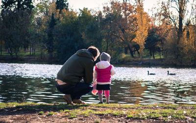 Rear view of man and child by lake by trees