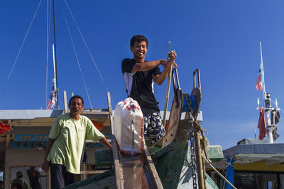 People standing on sailboat against clear blue sky