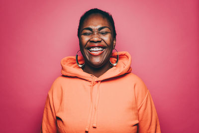 Cheerful mid adult woman wearing orange hooded shirt over pink background