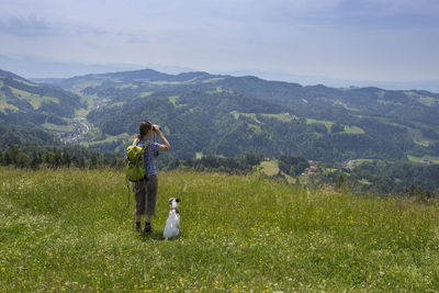 Woman standing with dog on grass against sky