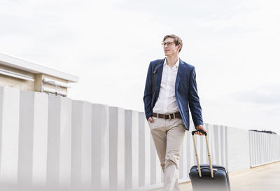 Confident businessman with rolling suitcase walking at parking garage