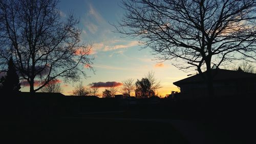 Silhouette bare trees and buildings against sky during sunset